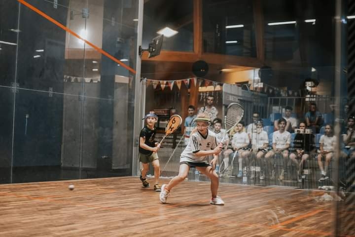 Dwie zawodniczki juniorki w squasha podczas gry, w tle widownia.