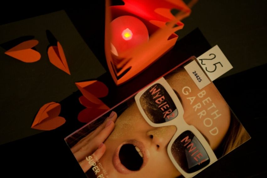 Okładka książki 'Wybierz mnie!', obok paląca się świeczka