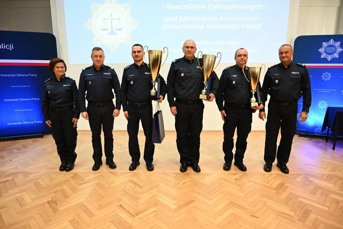 Sześcioro funkcjonariuszy Policji w umundurowaniu stoi na scenie, trzech z nich trzyma puchary podczas uroczystości w Centrum Szkolenia Policji w Legionowie.